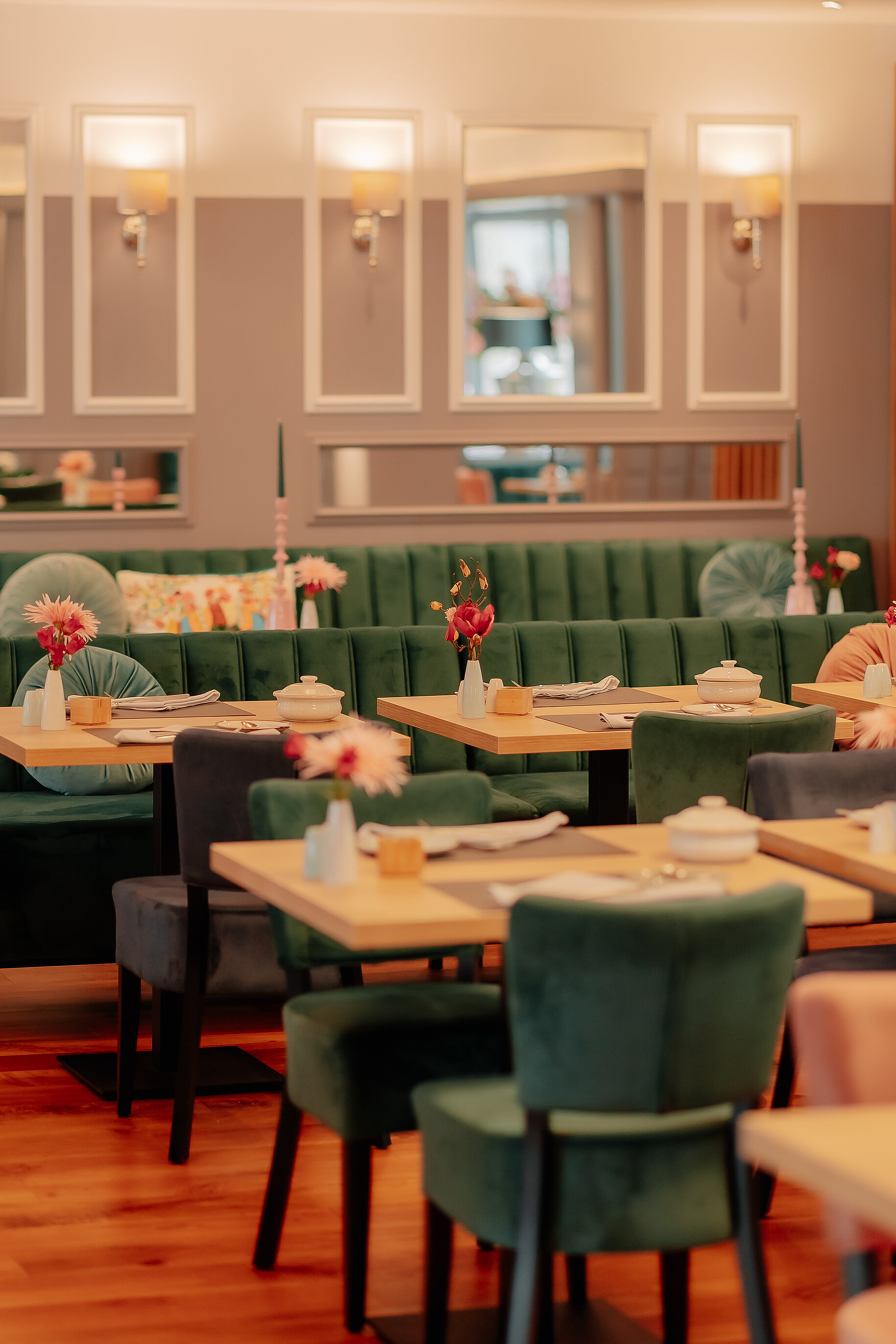 Detailaufnahme des modern gestalteten Frühstücksbereichs mit grünen Samtstühlen und frischen Blumen auf den Tischen im Stadthotel Borken